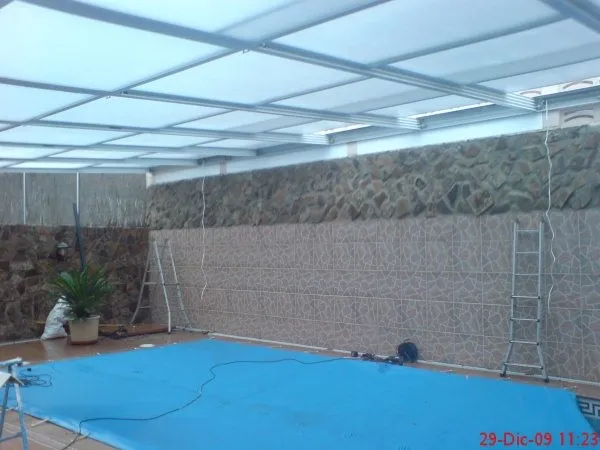 Vista interior de cubierta para piscina con cerramiento de aluminio y muros de piedra