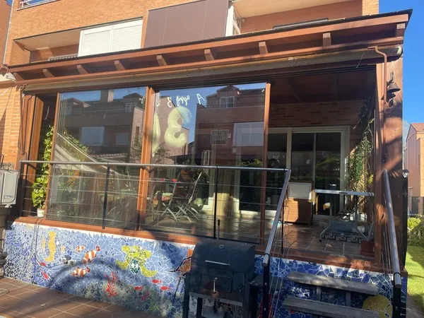 Porche y cerramiento de madera y cristal con barandilla metálica en zona de jardín