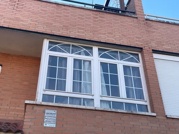 Cerramiento de ventana exterior con arco superior y persianas en fachada de ladrillo visto