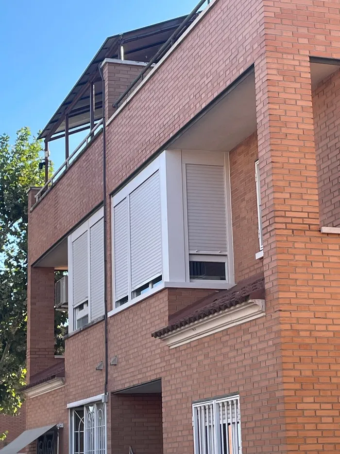 Cerramiento acristalado de esquina con persianas integradas en terraza de edificio residencial