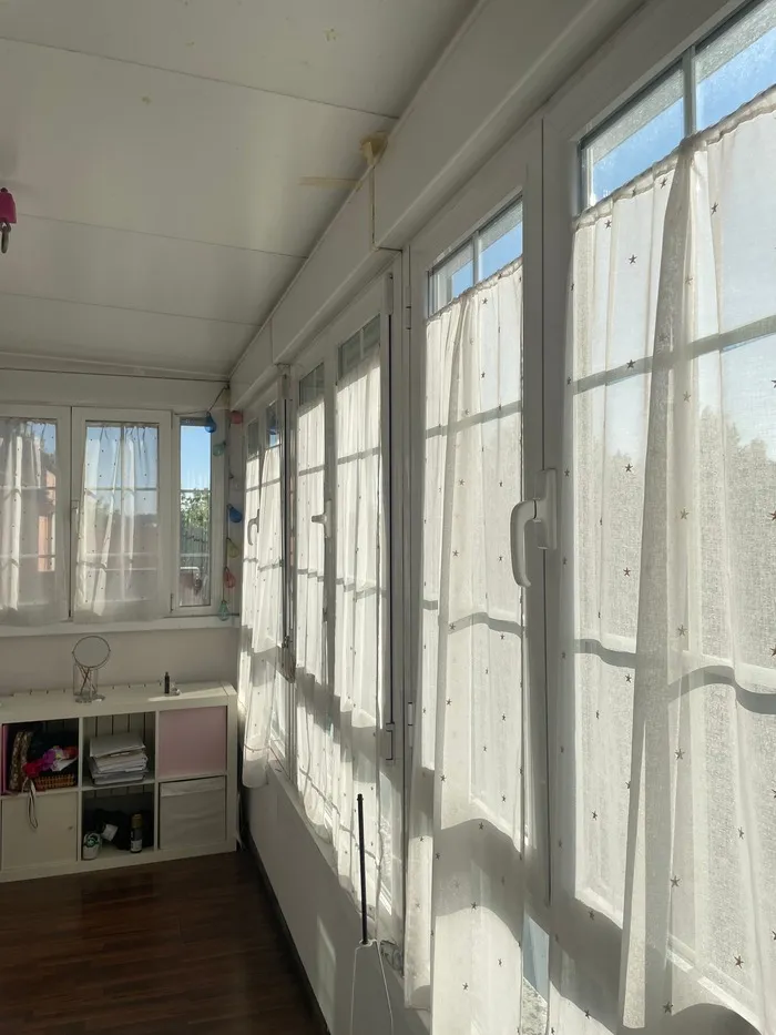 Cerramiento de terraza acristalado con perfilería blanca y cortinas en vivienda