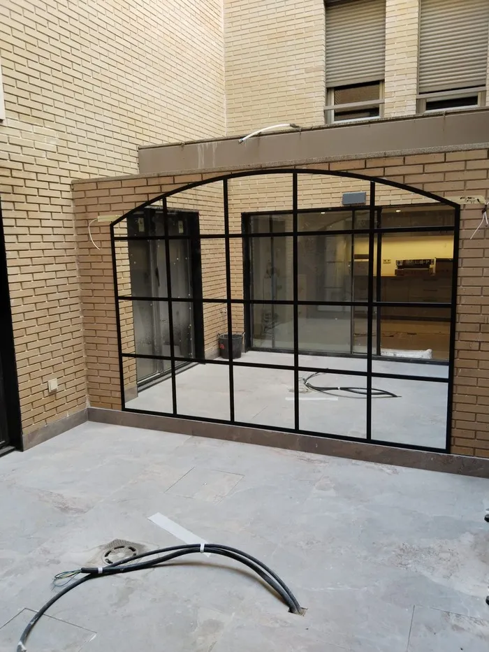 Estructura de cerramiento metálico negro con grandes ventanales en patio exterior